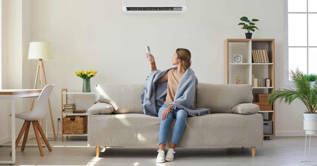 Woman adjusting a wall-mounted heat pump with a remote from her sofa