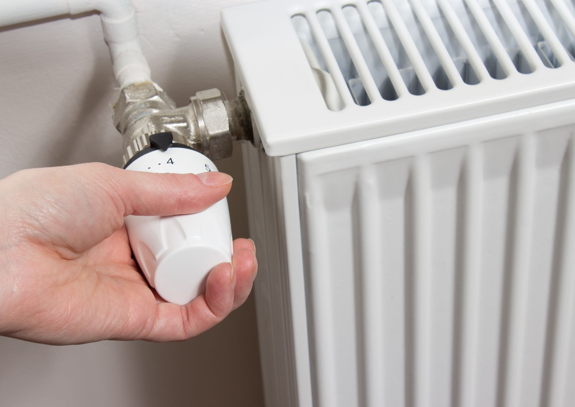 Hand turning down a radiator valve to save energy in winter
