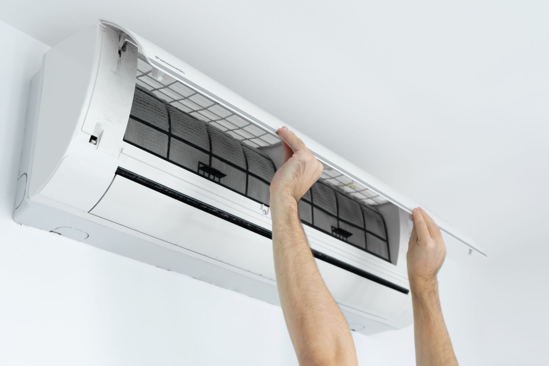 Technician removing the filter panel from a wall-mounted AC unit