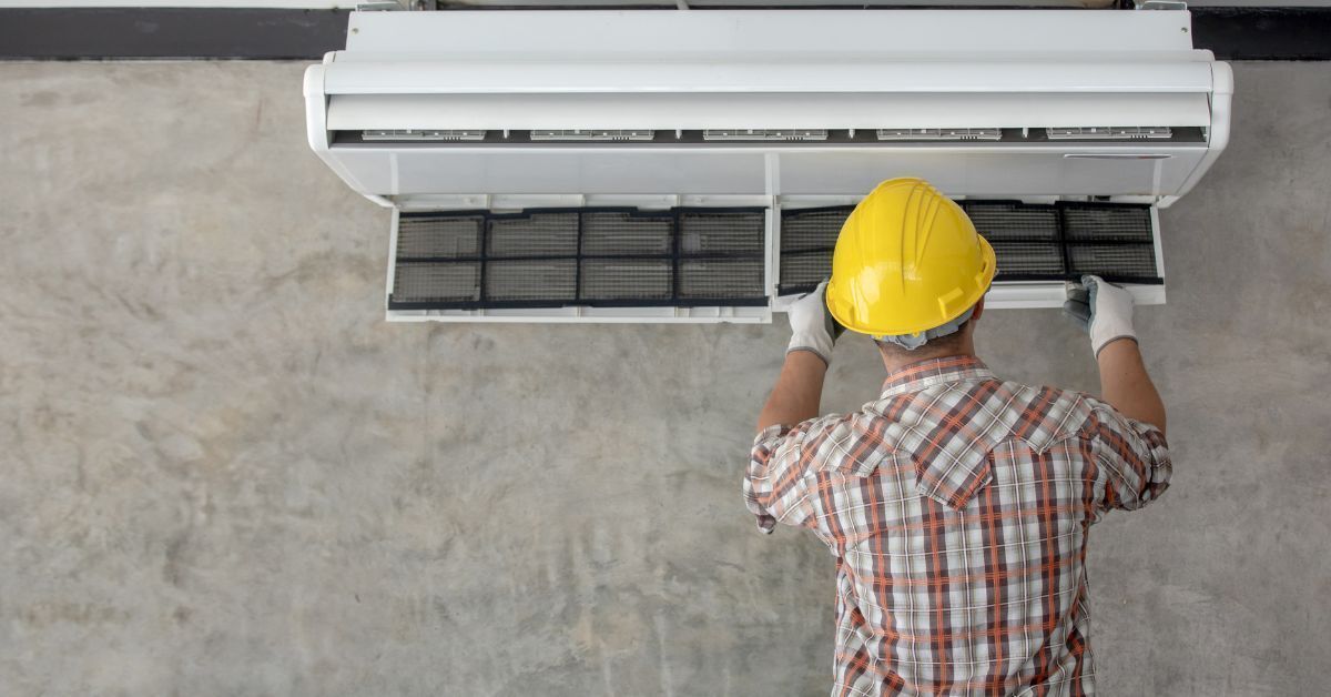 Technician in a hard hat servicing a wall-mounted air conditioner